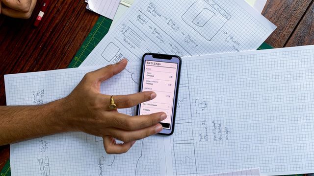 Hand bedient einen App-Prototyp auf dem Smartphone über handgezeichneten UI-Skizzen