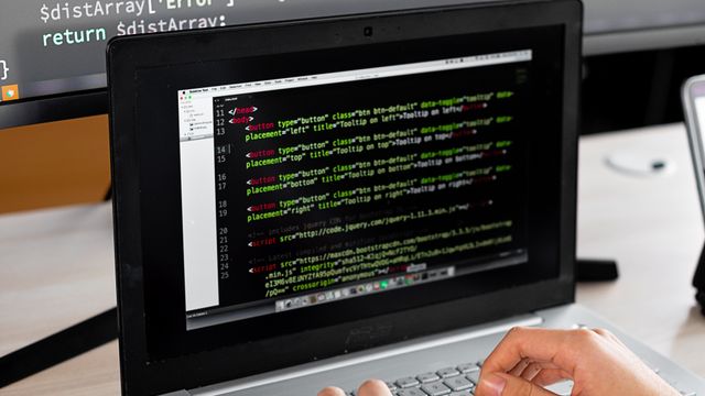 Entwickler arbeitet am Laptop mit dunklem Code-Editor und zweitem Monitor