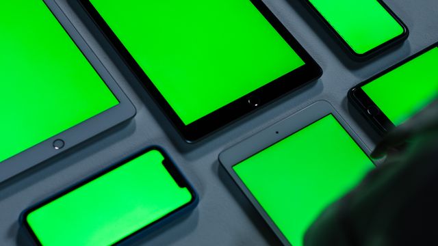 Mehrere Smartphones und Tablets mit leuchtenden Bildschirmen nebeneinander auf einem Tisch