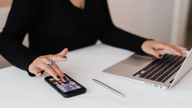 Frau nutzt am Schreibtisch gleichzeitig Smartphone und Laptop